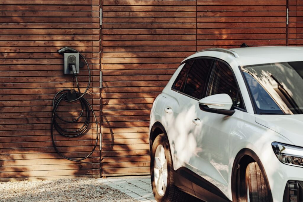 Borne de recharge murale et câble enroulé à côté d’une voiture blanche devant un bardage en bois.
