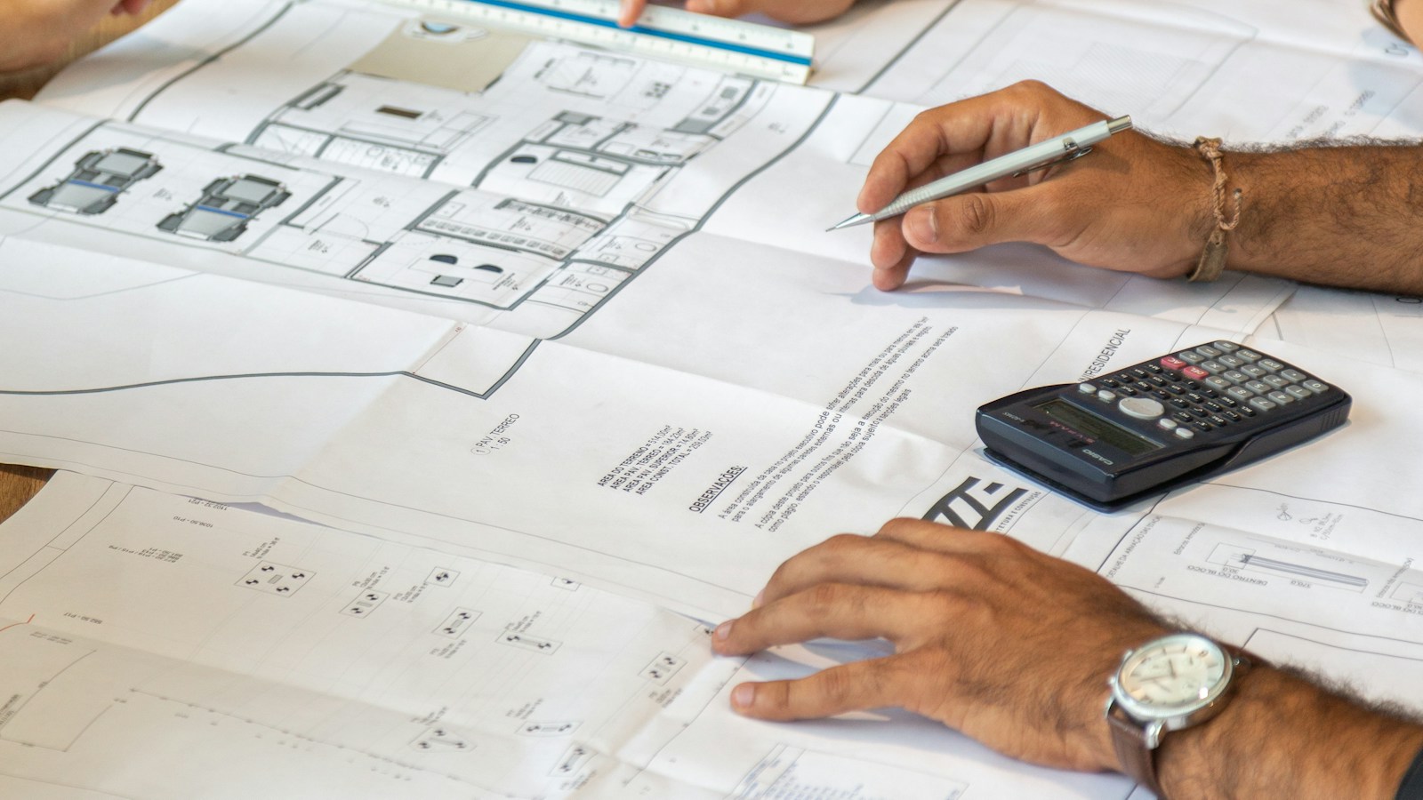 Des mains examinent des plans de logement, avec une calculatrice posée sur la table.