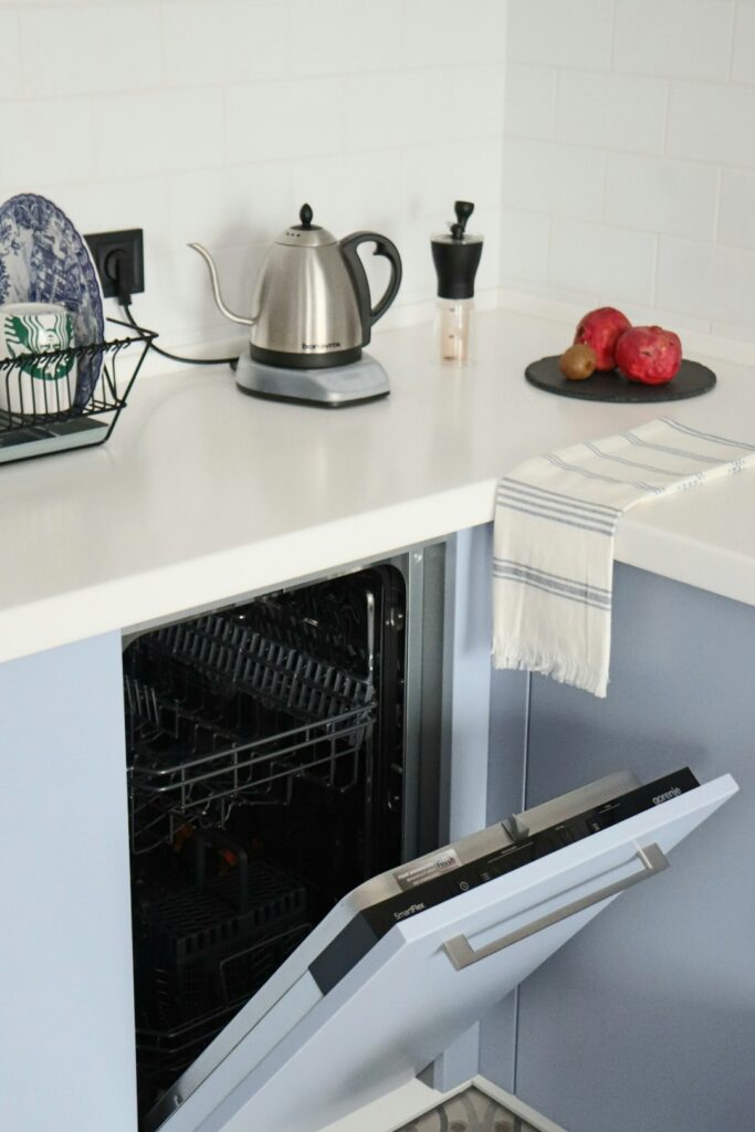 Lave-vaisselle ouvert sous un plan de travail avec une bouilloire électrique dans une cuisine lumineuse.