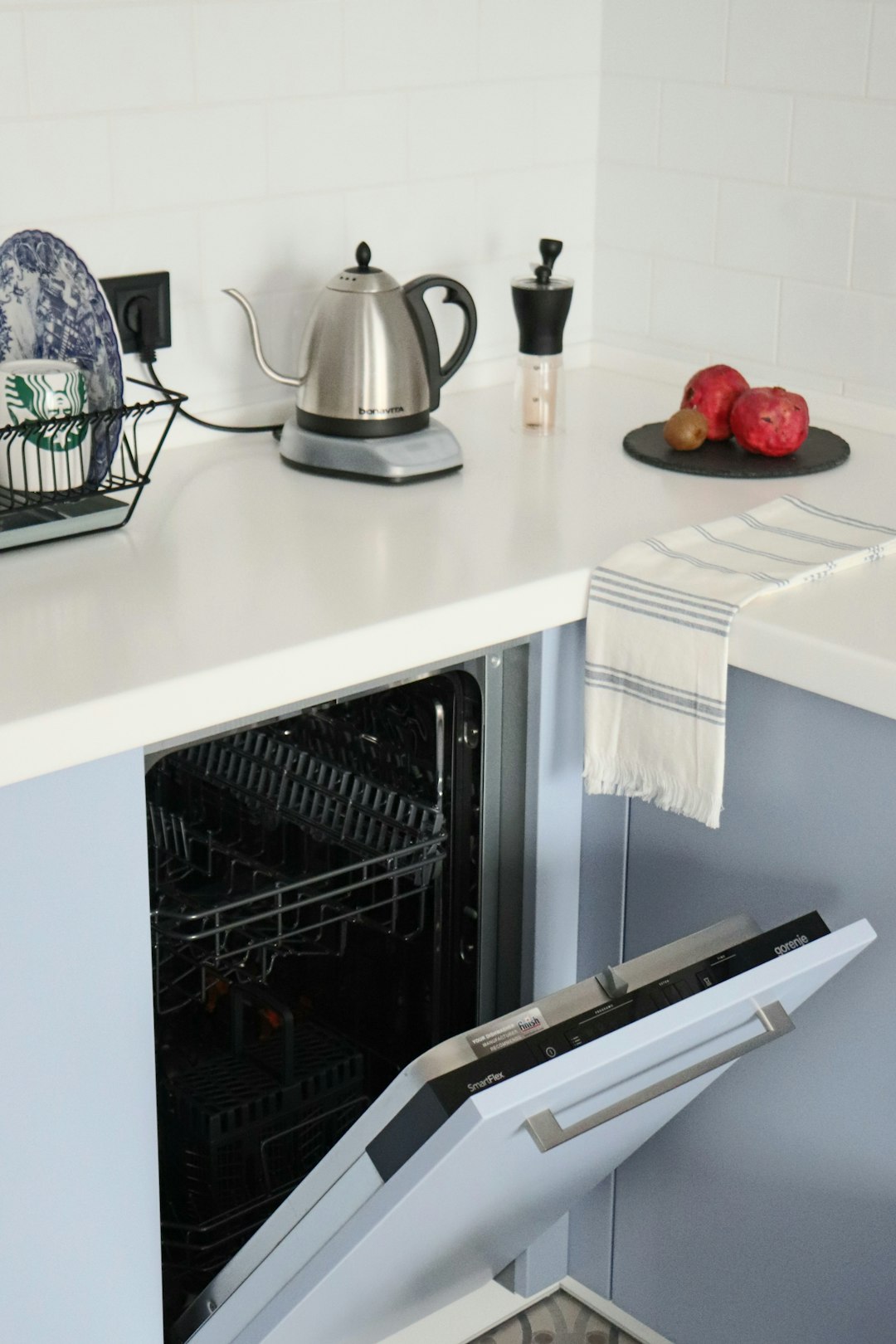 Lave-vaisselle ouvert sous un plan de travail avec une bouilloire électrique dans une cuisine lumineuse.