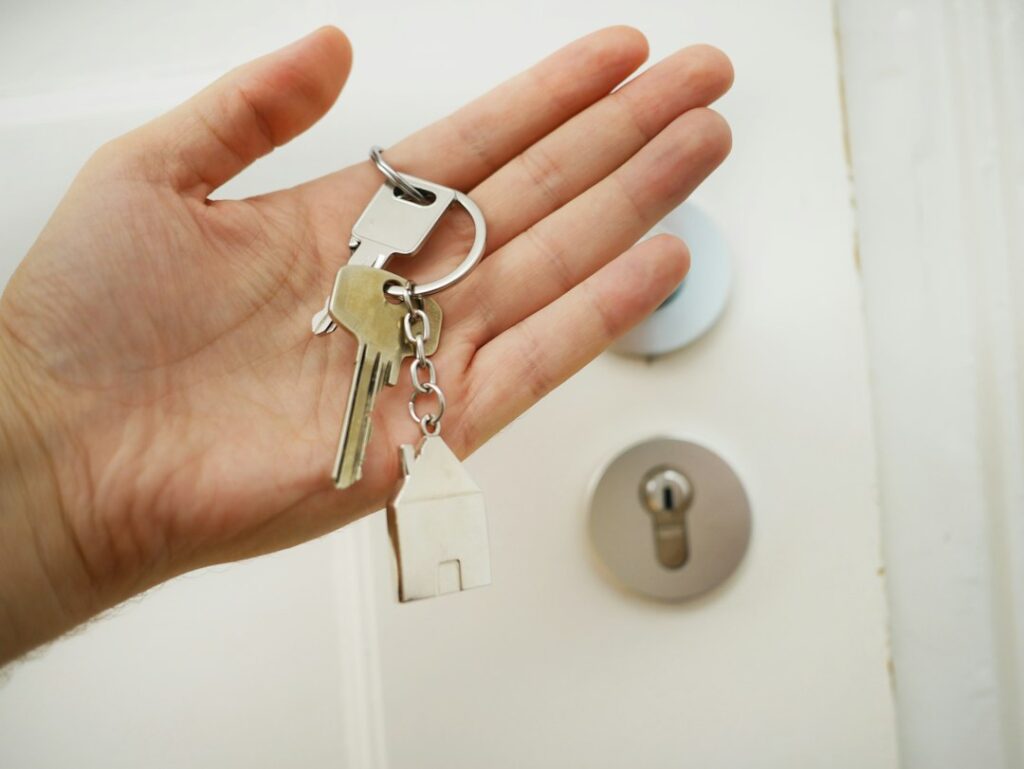 Main tenant des clés et un porte-clés en forme de maison devant une porte blanche.