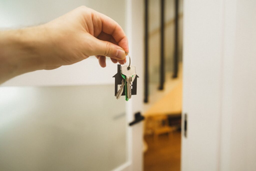 Main tenant un trousseau de clés devant une porte ouverte