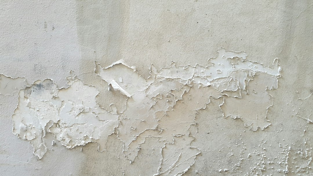 Peinture blanche écaillée et marques grisâtres sur un mur.