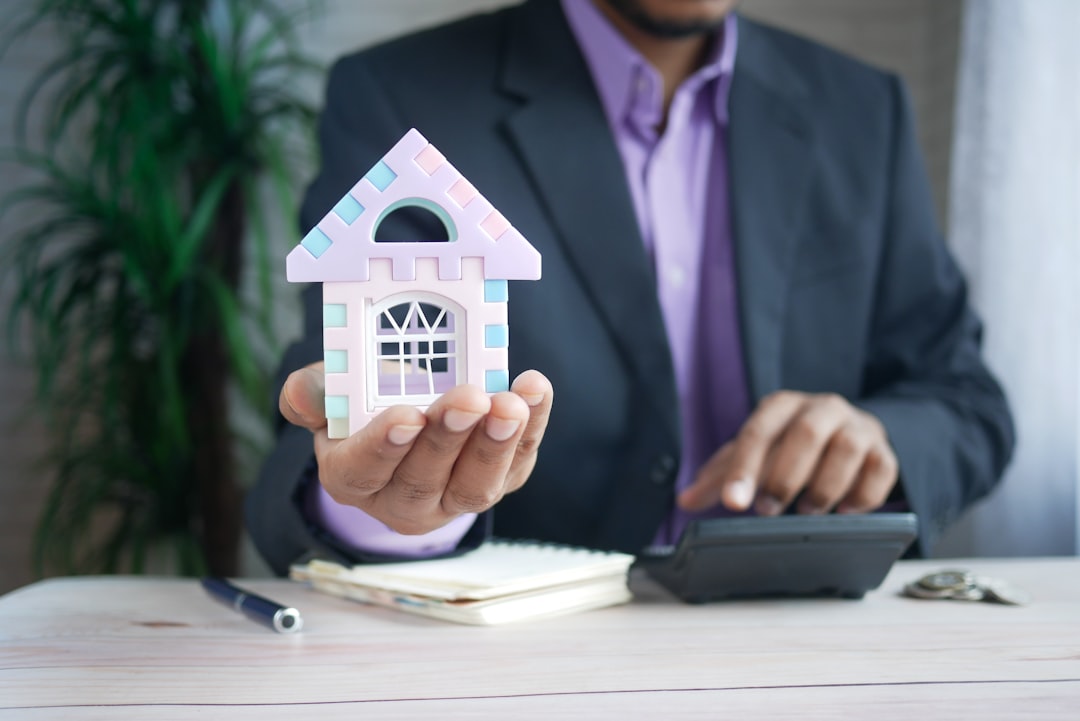 Personne tenant une maquette de maison devant une calculatrice et un carnet.