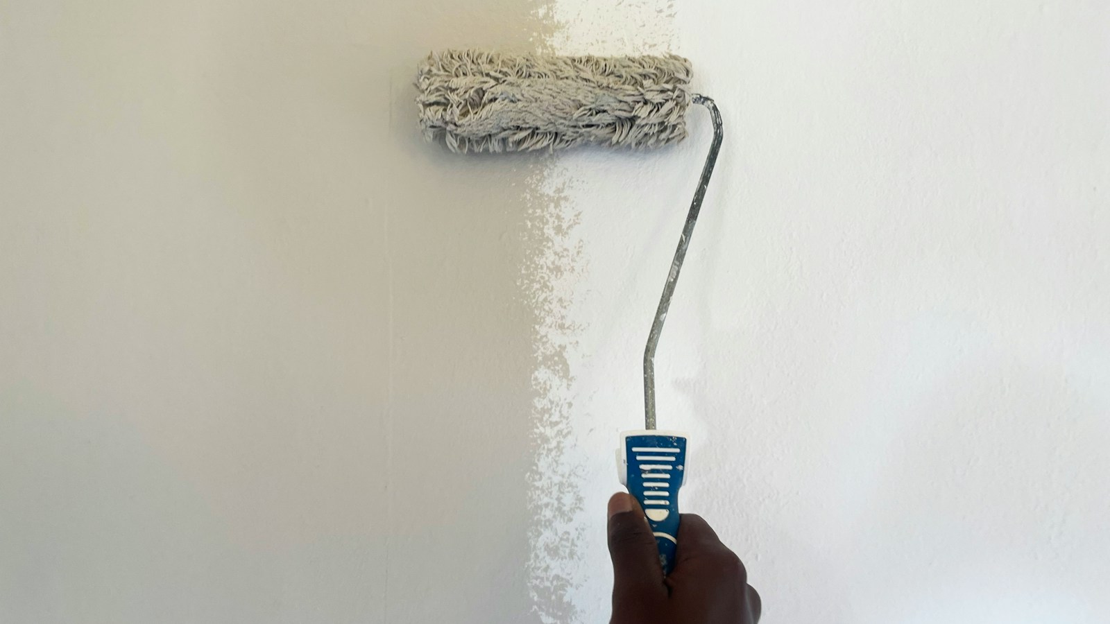 Une main passe un rouleau de peinture claire sur un mur intérieur.